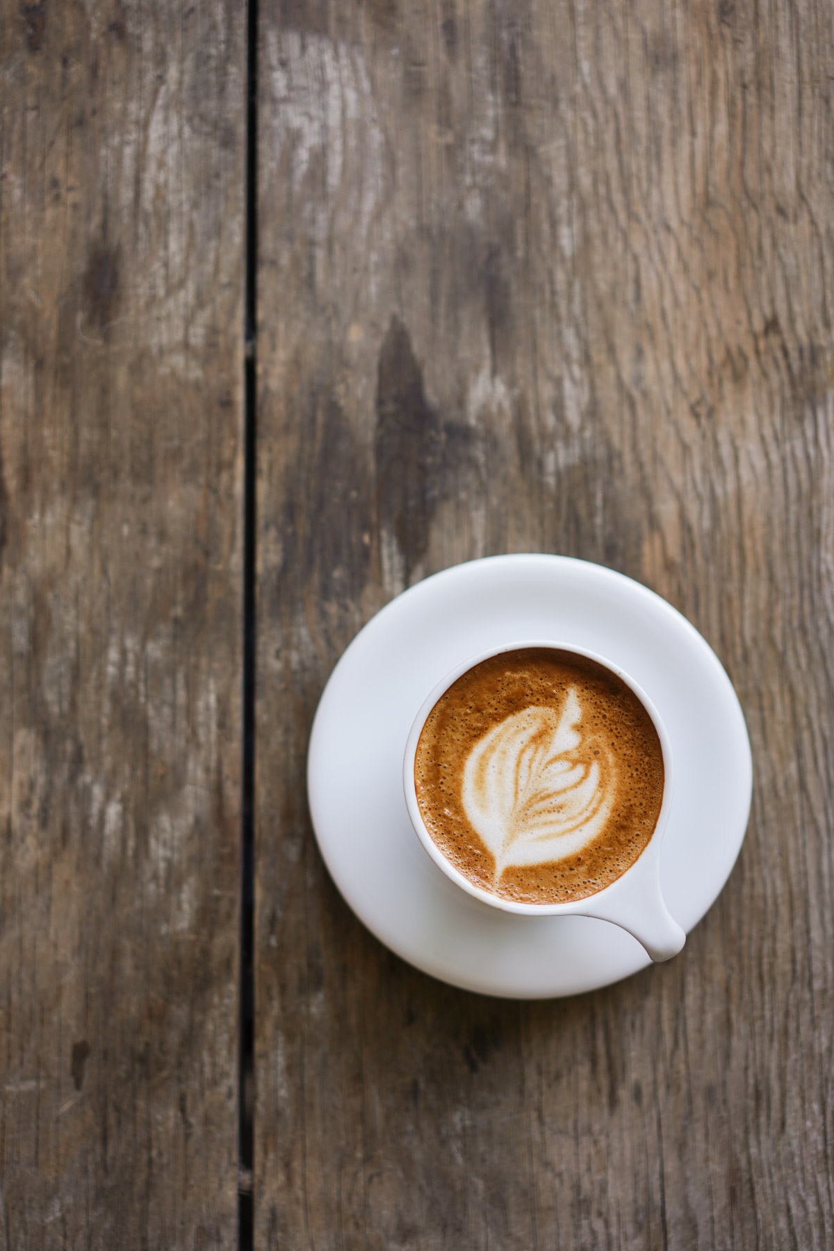 Artisan latte art served with cup and saucer on rustic wood table at a specialty cafe in Colonia Cacho Tijuana